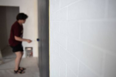 Patenli duvar boyası. İşçi duvarı boyar, evi elden geçirir, beyaz tuğlalara odaklanır. Ressam iş başında. Ev yenilenmesi
