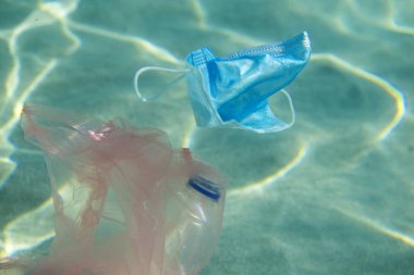 Okyanus kirliliği. Kişisel koruyucu maske, plastik şişe ve su altında çanta. Koronavirüs salgını sırasında cerrahi maskelerin aşırı kullanımı ve uygunsuz atık imhası sonucu.