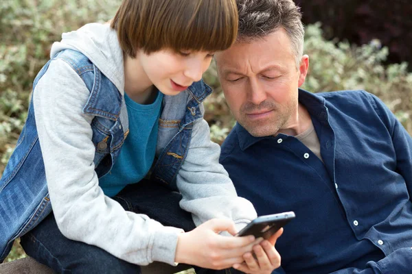 父亲带着儿子用智能手机在户外一起 年轻男孩与他的父亲在春天公园 — 图库照片