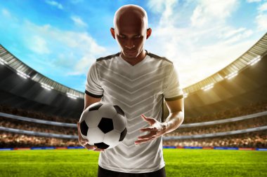 Futbol oyuncusu stadyumda top tutuyor.