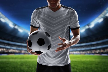 Futbol oyuncusu stadyumda top tutuyor.