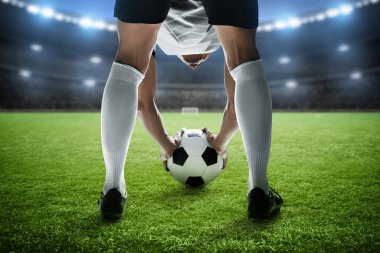 Futbol oyuncusu stadyumda top tutuyor.