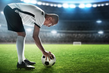 Futbol oyuncusu stadyumda top tutuyor.