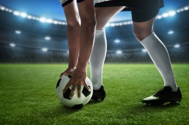 Futbol oyuncusu stadyumda top tutuyor.