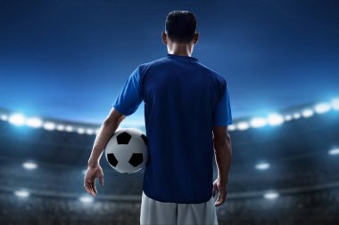 Futbol oyuncusu stadyumda top tutuyor.