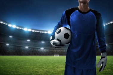 Futbol kalecisi stadyumda topu tutuyor.