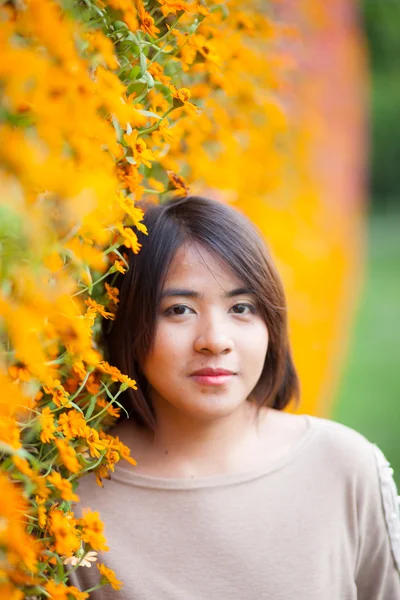 Portrait Asian woman standing near yellow flowers. — Stock Photo, Image