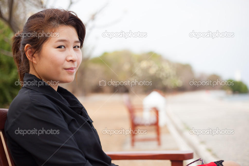 Asian women black shirt. Sitting on wooden bench.