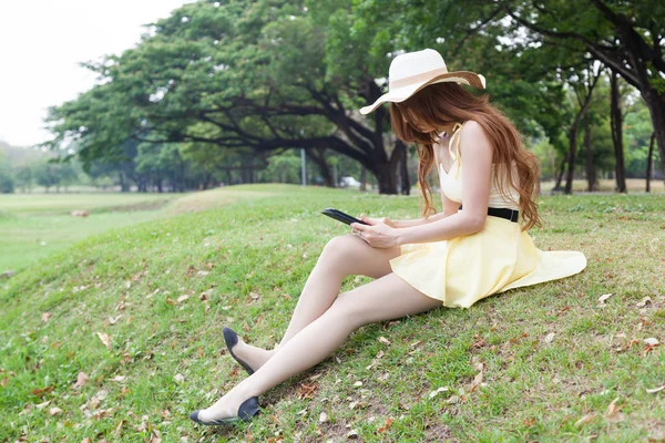 Mujer sentada en la hierba y usando una tableta . —  Fotos de Stock