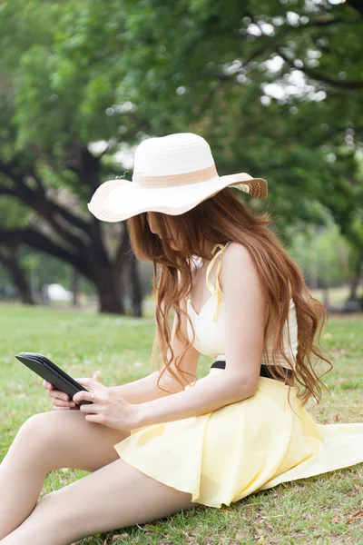 Femme assise sur l'herbe et utilisant une tablette . — Photo