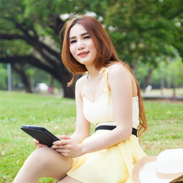 Wanita yang duduk di halaman memegang tablet . — Stok Foto