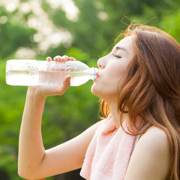 Mujer sentada cansada y bebiendo agua después del ejercicio . — Foto de Stock