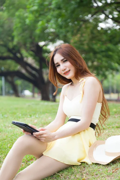 Kobieta siedzi na trawniku trzymając tabletkę. — Zdjęcie stockowe