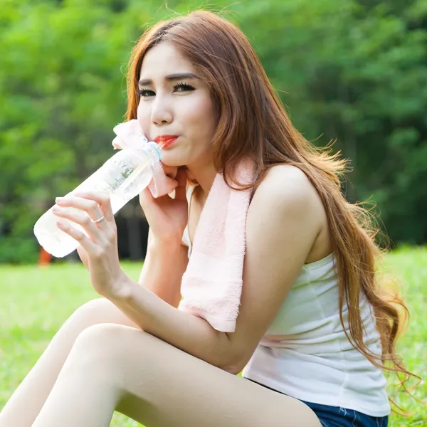 Mujer sentada cansada y bebiendo agua después del ejercicio . — Foto de Stock