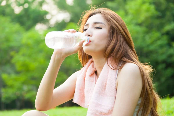 Mujer sentada cansada y bebiendo agua después del ejercicio . — Foto de Stock