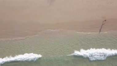 Kumsalda koşan bir adam. Üst görüntü hava aracı görüntüleri kumlu sahilde deniz dalgaları kırılıyor. Sınıflandırılmamış video.