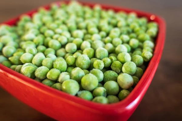 Gefrorene frostige grüne Erbsen in roter Keramikschale Nahaufnahme — Stockfoto