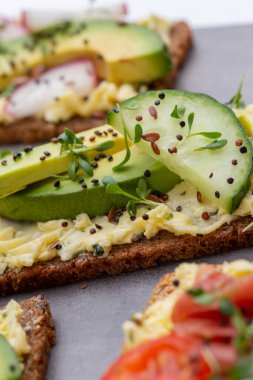Krem peynirli, sebzeli ve salamlı mini sandviçler. Salatalıklı sandviçler, turp, domates, gri arka planda salam, üst manzara. Düz yatıyordu.
