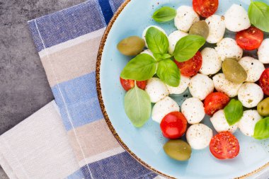 Kiraz domatesleri, mozzarella peyniri, fesleğen ve baharatlar gri tahta üzerinde. İtalyan geleneksel Caprese salata malzemeleri. Akdeniz yemekleri.