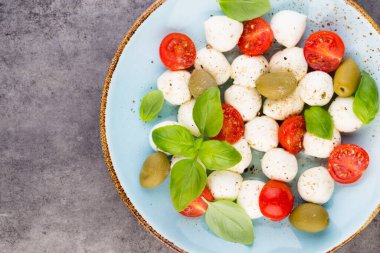 Kiraz domatesleri, mozzarella peyniri, fesleğen ve baharatlar gri tahta üzerinde. İtalyan geleneksel Caprese salata malzemeleri. Akdeniz yemekleri.