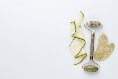 Gua Sha yüz masajı aletleri ve salatalık. Pastel arka planda kuvars yeşim silindiri. Evde yaş, kaldırma ve tonlama karşıtı tedavi. 