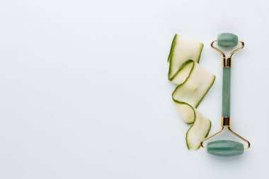 Gua Sha yüz masajı aletleri ve salatalık. Pastel arka planda kuvars yeşim silindiri. Evde yaş, kaldırma ve tonlama karşıtı tedavi. 