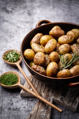 Kavrulmuş patatesle dolu tava sade ahşap masada atılıyor. İçlerinde çiğ patates, biberiye, dereotu, tuz, biber ve sarımsak var.. 