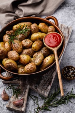 Kavrulmuş patatesle dolu tava sade ahşap masada atılıyor. İçlerinde çiğ patates, biberiye, dereotu, tuz, biber ve sarımsak var.. 