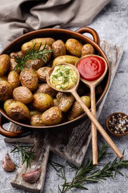 Kavrulmuş patatesle dolu tava sade ahşap masada atılıyor. İçlerinde çiğ patates, biberiye, dereotu, tuz, biber ve sarımsak var.. 