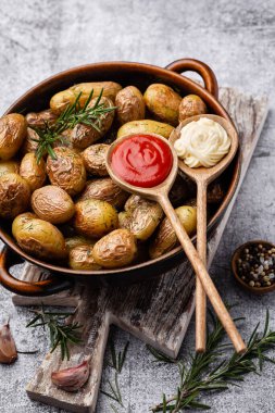 Kavrulmuş patatesle dolu tava sade ahşap masada atılıyor. İçlerinde çiğ patates, biberiye, dereotu, tuz, biber ve sarımsak var.. 