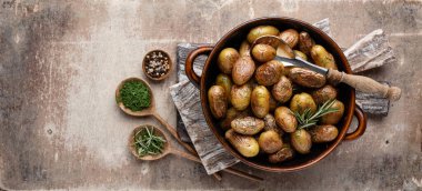 Kavrulmuş patatesle dolu tava sade ahşap masada atılıyor. İçlerinde çiğ patates, biberiye, dereotu, tuz, biber ve sarımsak var.. 