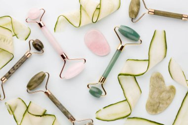 Gua Sha yüz masajı aletleri ve salatalık. Pastel arka planda kuvars yeşim silindiri. Evde yaş, kaldırma ve tonlama karşıtı tedavi. 
