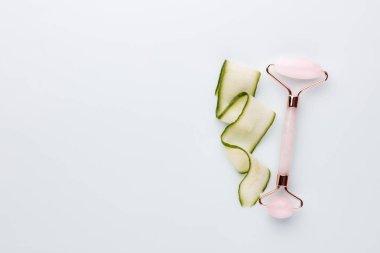 Gua Sha yüz masajı aletleri ve salatalık. Pastel arka planda kuvars yeşim silindiri. Evde yaş, kaldırma ve tonlama karşıtı tedavi. 
