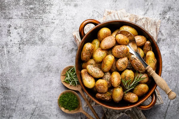 Kavrulmuş patatesle dolu tava sade ahşap masada atılıyor. İçlerinde çiğ patates, biberiye, dereotu, tuz, biber ve sarımsak var.. 