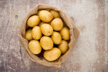 Ahşap arka planda taze çiğ patates çuvalı..