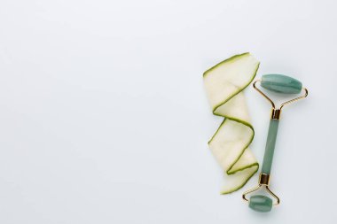 Gua Sha yüz masajı aletleri ve salatalık. Pastel arka planda kuvars yeşim silindiri. Evde yaş, kaldırma ve tonlama karşıtı tedavi. 