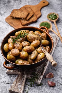 Kavrulmuş patatesle dolu tava sade ahşap masada atılıyor. İçlerinde çiğ patates, biberiye, dereotu, tuz, biber ve sarımsak var.. 