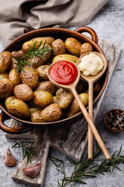 Kavrulmuş patatesle dolu tava sade ahşap masada atılıyor. İçlerinde çiğ patates, biberiye, dereotu, tuz, biber ve sarımsak var.. 