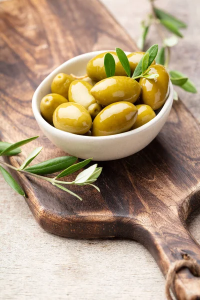 Green olives on gray background. Olives in wooden bowls over wooden cutting board and fresh olive leaves. Copy space.
