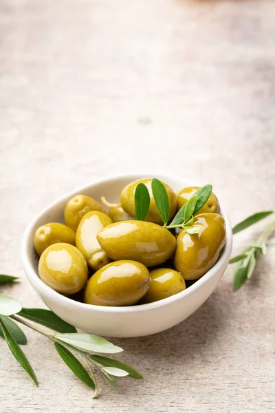 Green olives on gray background. Olives in wooden bowls over wooden cutting board and fresh olive leaves. Copy space.