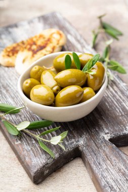 Gri arka planda yeşil zeytin. Tahta kesme tahtası ve taze zeytin yaprakları üzerinde ahşap kaselerde zeytinler. Boşluğu kopyala.