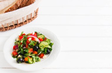 Beyaz tabakta sebze salatası ve sepette ekmek..