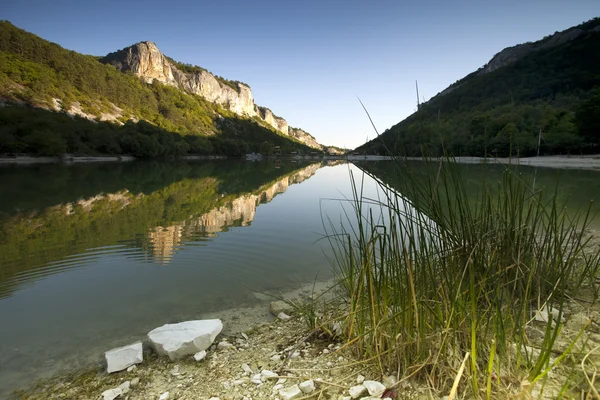 Gölün kıyısında kayalık ve Yeşil dağlar yansıtacak — Stok fotoğraf
