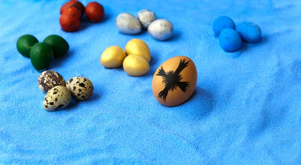 Colorful eggs and cross on blue sand background — Stock Photo, Image