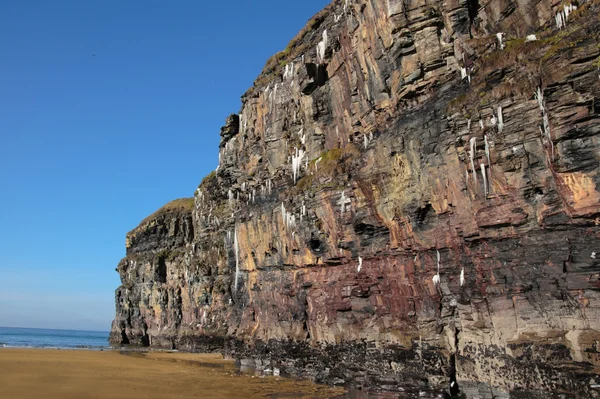 Ijspegels die smelten op een rotswand strand — Stockfoto