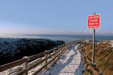 Warning sign on a winter snow cliff walk clipart