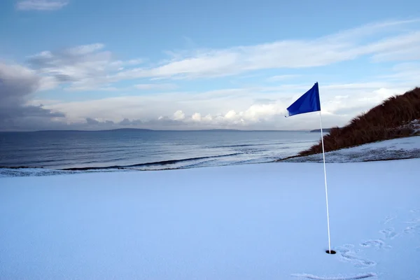 Campo de golfe verde com neve e uma bandeira azul Fotografia De Stock