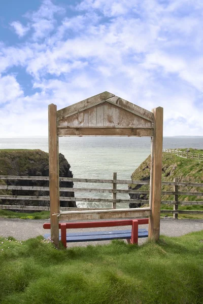 Un banco rojo de madera enmarcado con una vista al mar — Foto de Stock