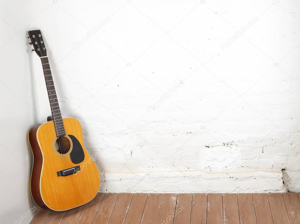 Musical instrument - Classic acoustic guitar on a white brick background and wooden floor.