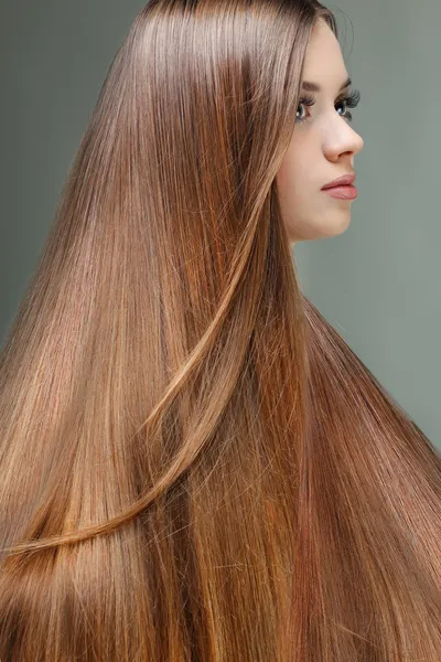 Portret van mooi meisje met lange haren, op een grijze achtergrond, emoties, cosmetica — Stockfoto